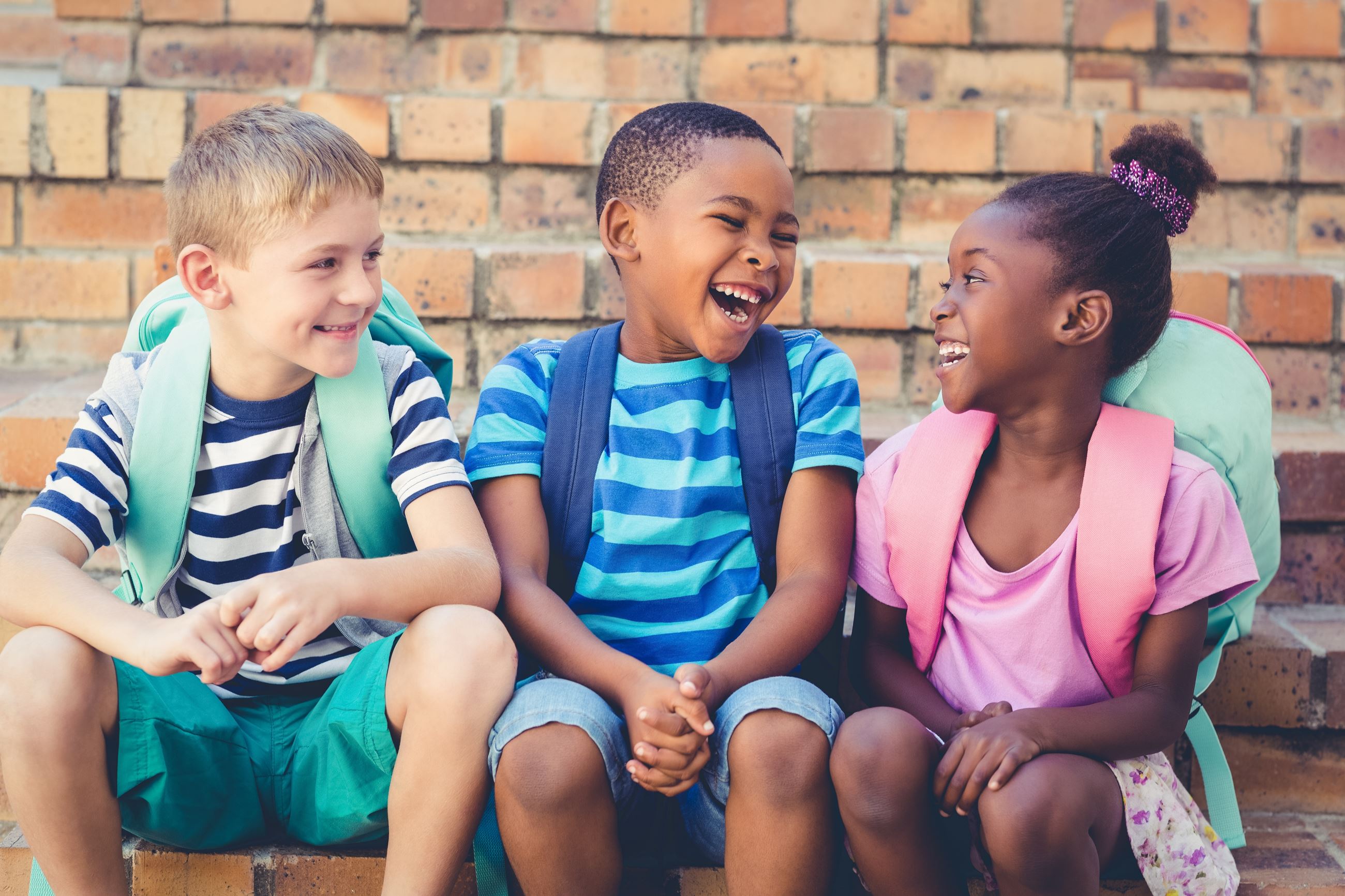 Image of laughing children wearing backpacks sitting on a step together